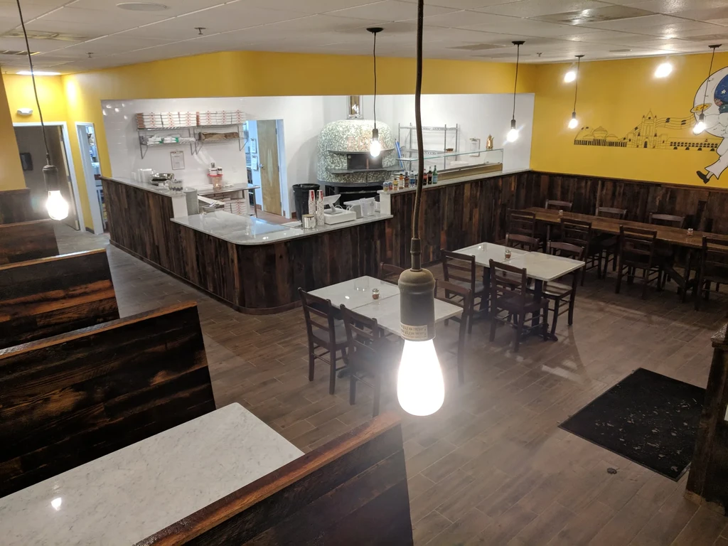 Interior of a pizza restaurant with varied seating and prominent stone oven.