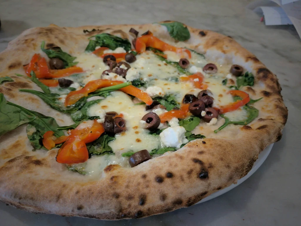 Freshly baked Neapolitan pizza with olives, peppers, spinach, and cheeses.