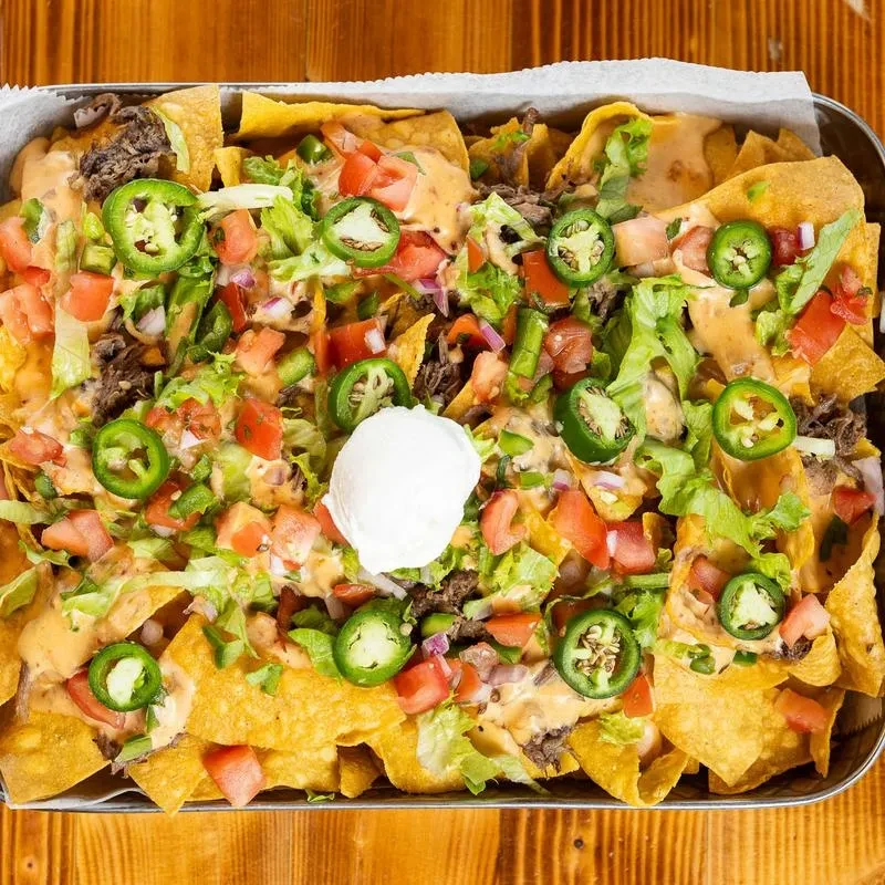 Overhead view of loaded nachos with cheese, meat, vegetables, and sour cream.