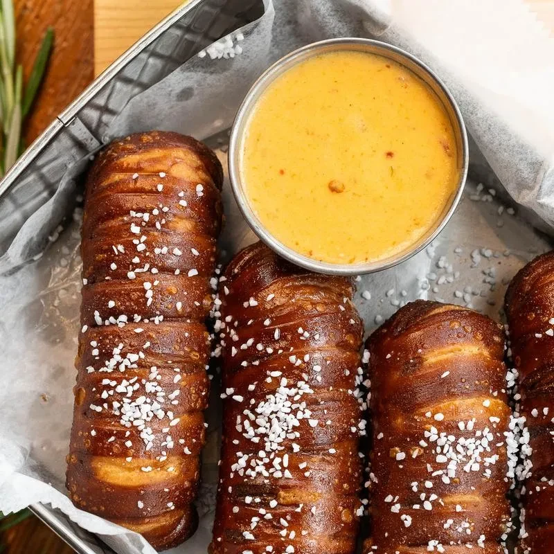 Overhead of four salted pretzel sticks and cheese sauce in a metal basket.