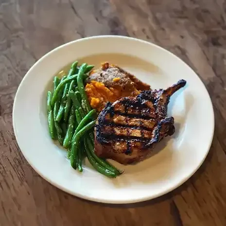 Grilled pork chop, green beans, and sweet potato purée on a white plate.