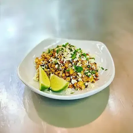 White bowl of Esquites with roasted corn, crumbled cheese, and lime.