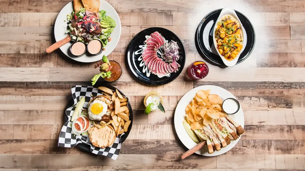 Overhead flat lay of diverse food and drinks on a rustic wooden table.