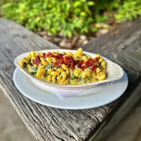 Creamy cheese pasta with green vegetables and crispy bacon on a wooden surface.