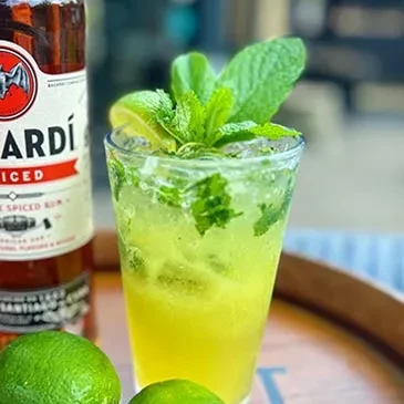 Green cocktail with mint, lime, ice, and Bacardi Spiced Rum bottle.