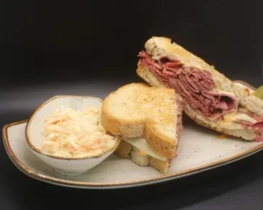 Sliced deli meat sandwich, cut in half, and coleslaw.