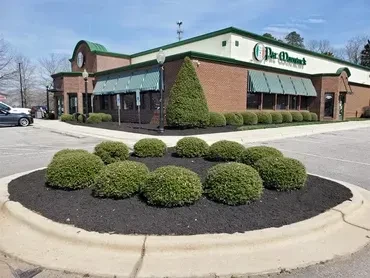 Sunny exterior of a brick restaurant with a green roof and landscaping.