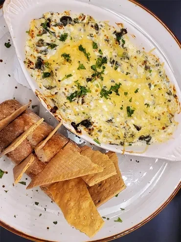 Overhead baked dip with melted cheese, parsley, baguette, and crackers.
