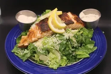 Grilled salmon Caesar salad with lemon wedges and side dressing.