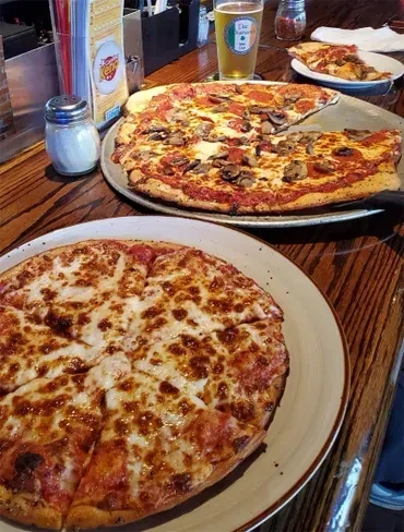 Two pizzas, cheese and pepperoni, partially eaten, with a beer.