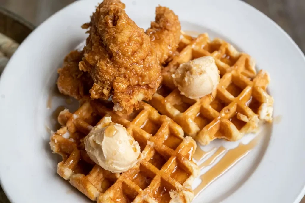 Plate of golden chicken and waffles with butter and syrup.