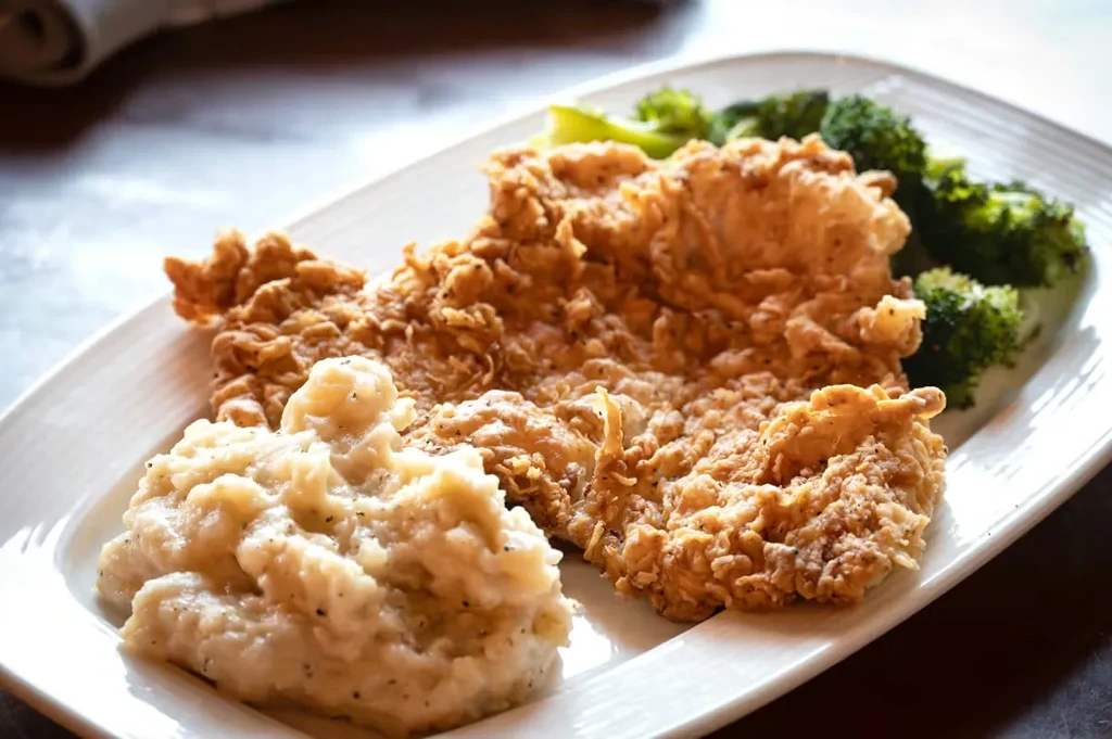 Crispy fried chicken, mashed potatoes, and broccoli on a white plate.