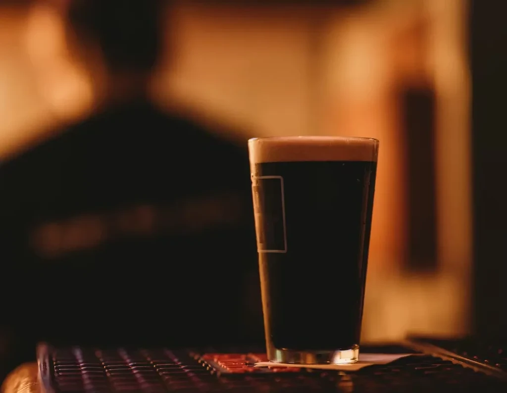 Tall glass of dark beer with creamy foam on a bar.