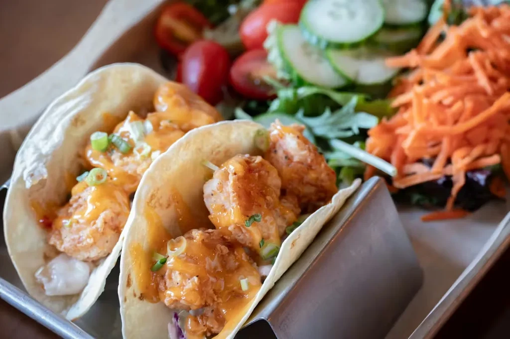 Two fried seafood tacos, orange sauce, green onions, and side salad.