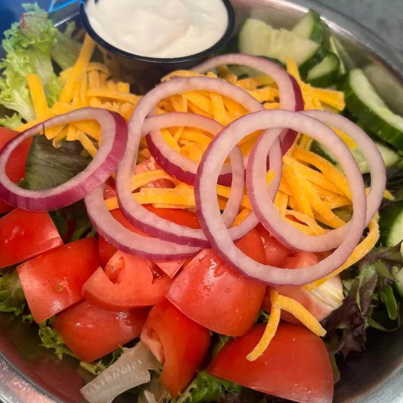 Fresh salad in metal bowl: lettuce, tomato, onion, cheddar, cucumber.