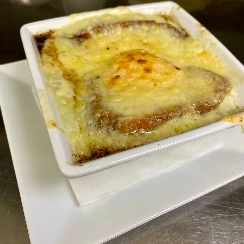 White bowl of French onion soup topped with bubbly, golden-brown melted cheese.