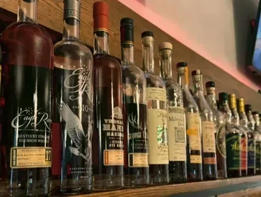 Various whiskey and bourbon bottles displayed on a wooden bar shelf.