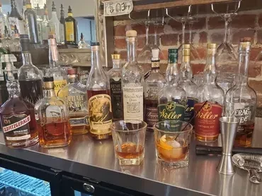 Well-stocked whiskey bar counter with two cocktails and bar tools.