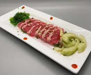 Tuna sashimi with seaweed salad, cucumber, and orange sauce on white plate.