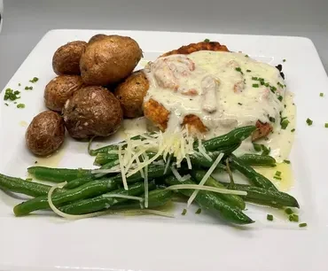 Dish with sauced protein, shrimp, roasted potatoes, and cheesy green beans.