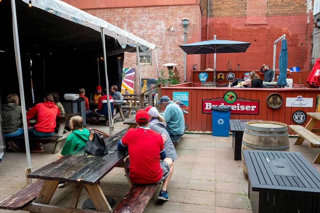 Busy outdoor beer garden with picnic tables, a bar, and people.
