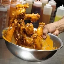 Orange-sauced chicken wings being tossed in a metal bowl.