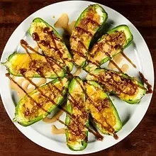 White plate with seven stuffed green vegetables and brown sauce.