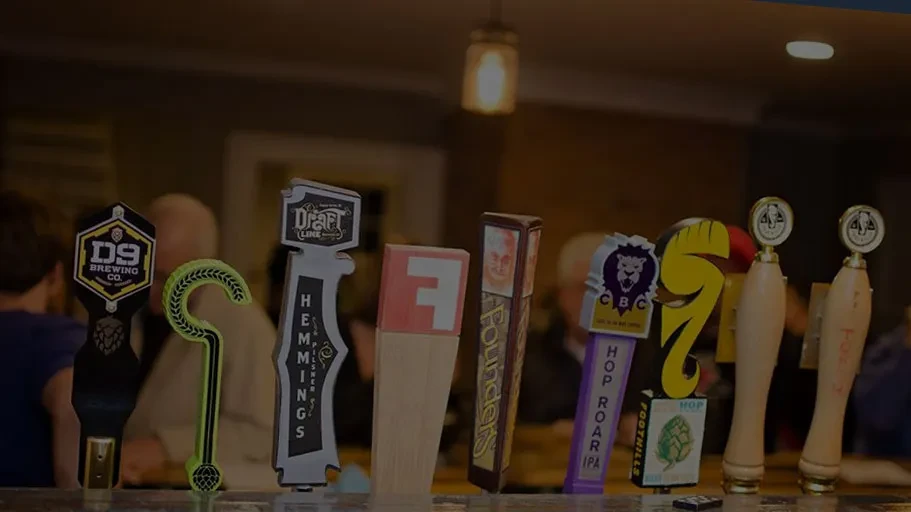 A row of distinct, branded beer tap handles at a bar.