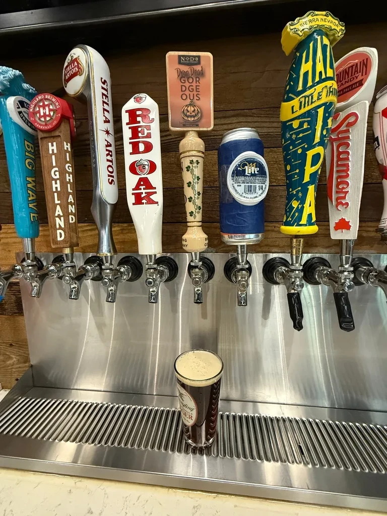 Eight distinct beer tap handles, a dark beer, on polished bar equipment.