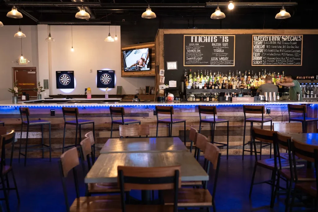 Modern bar interior with well-stocked bar, dartboards, and sports on TV.