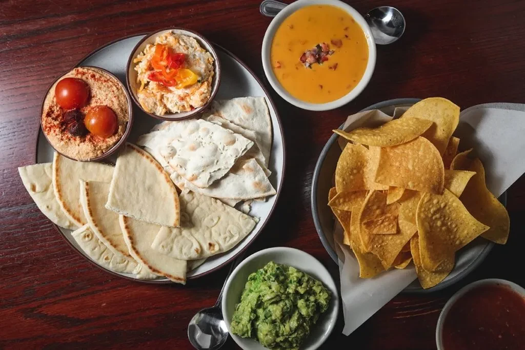Overhead shot of various dips, flatbread, and chips on a wooden table.