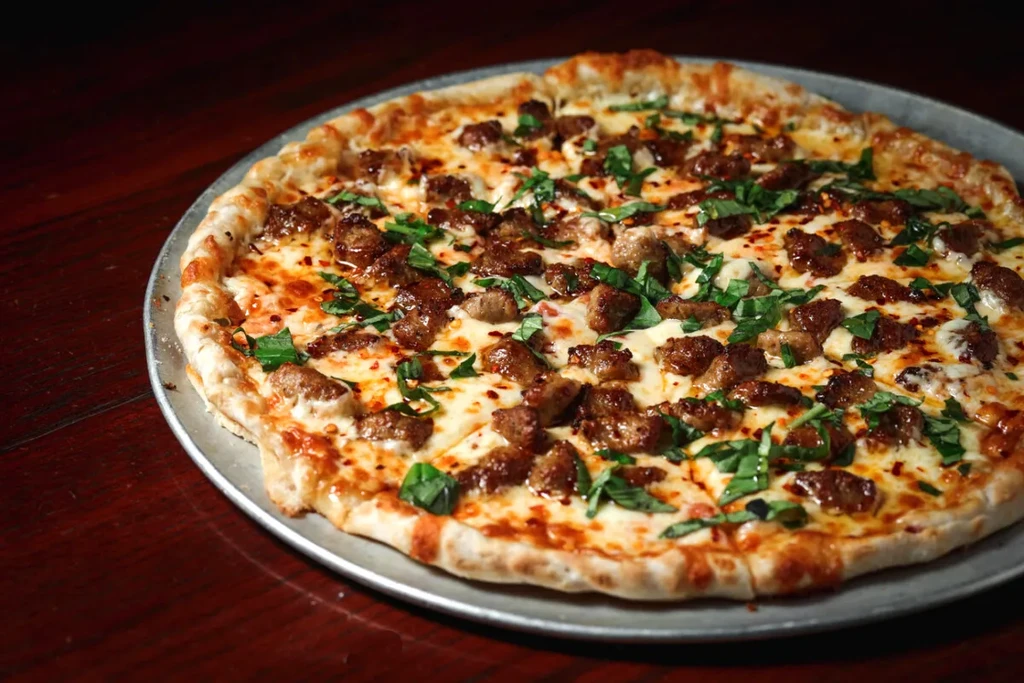 Pizza on pan with melted mozzarella, sausage, basil, red spice.