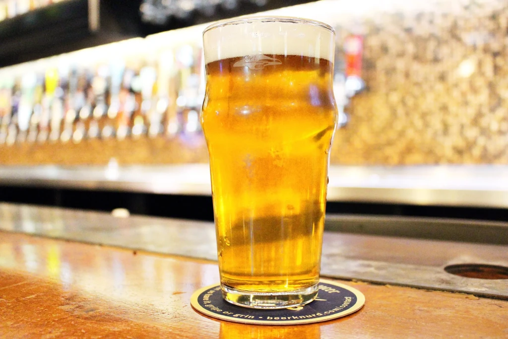Cold golden beer with foam on a bar, blurred taps background.