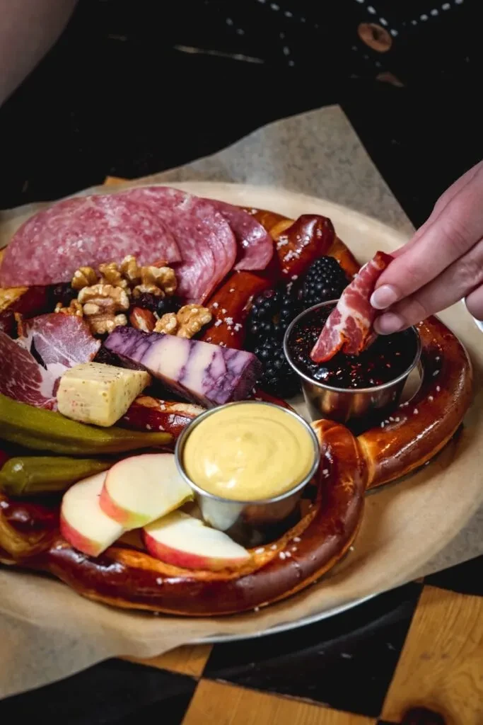Charcuterie board: pretzels, meats, cheeses, berries. Hand dipping meat.