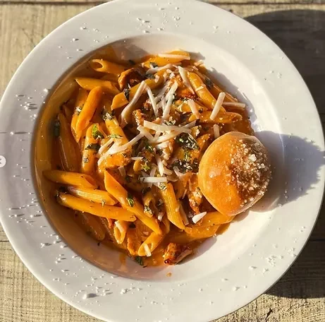 Penne pasta with creamy orange-red sauce, cheese, herbs, and side roll.
