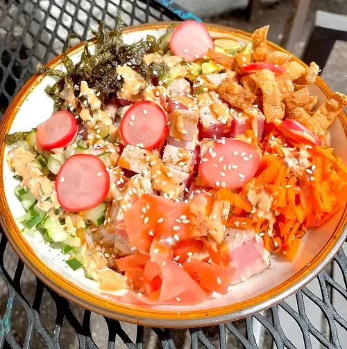 Vibrant poke bowl with raw fish, assorted vegetables, and pickled ginger.