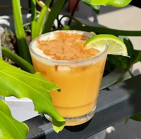 Golden-orange drink with foamy top, spice, lime slice, and ice.