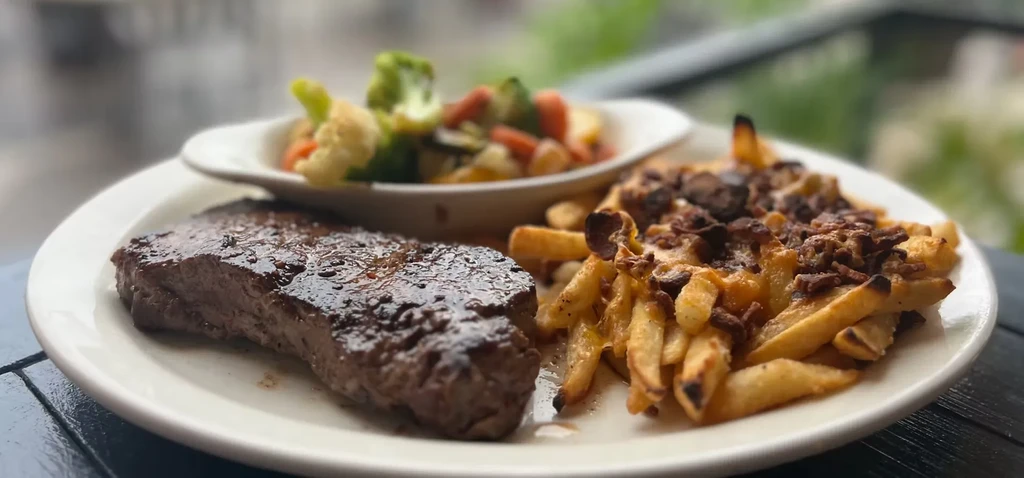 Steak, cheesy gravy fries, and mixed vegetables on an oval plate.