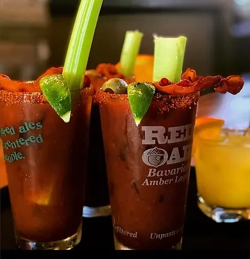 Two heavily garnished Bloody Mary cocktails on a bar.