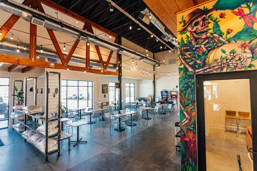 Wide industrial-rustic restaurant interior with seating, colorful mural, pinball machines.
