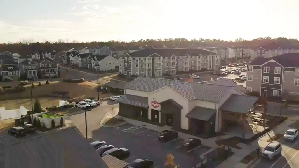 Aerial view of a modern suburban restaurant with parking, residential buildings, and pond.