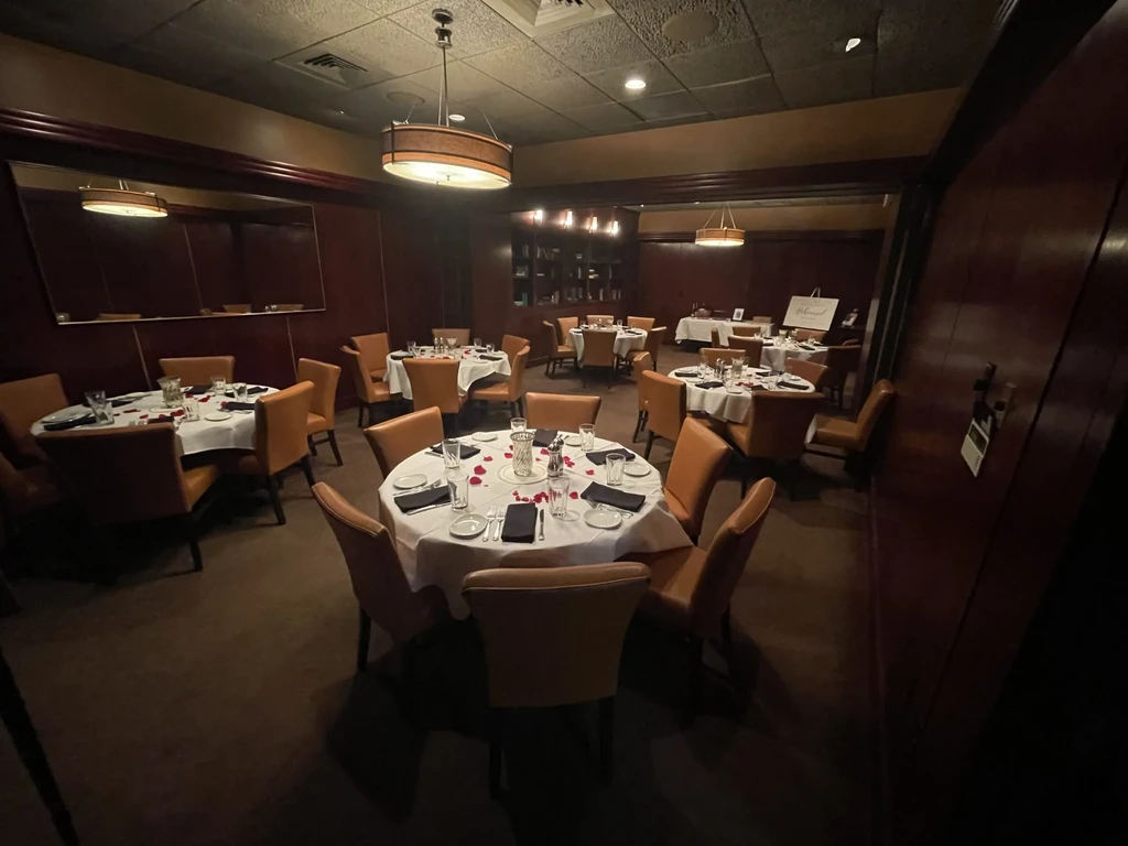 Intimate upscale dining room with dark wood, set tables, rose petals.