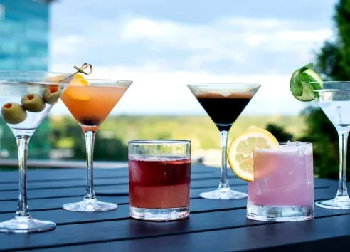 Six distinct alcoholic beverages on a dark outdoor table.