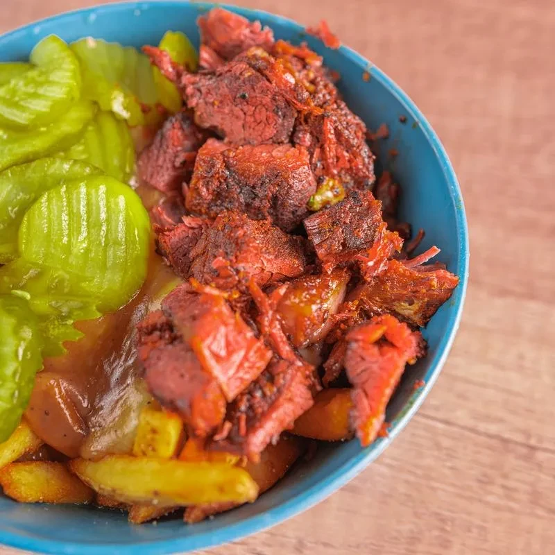 Teal bowl of loaded fries topped with pastrami, gravy, and pickles.