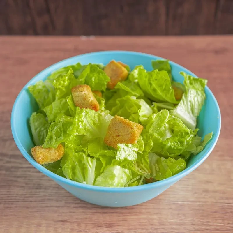 Fresh green salad with croutons in a light blue bowl on wood.