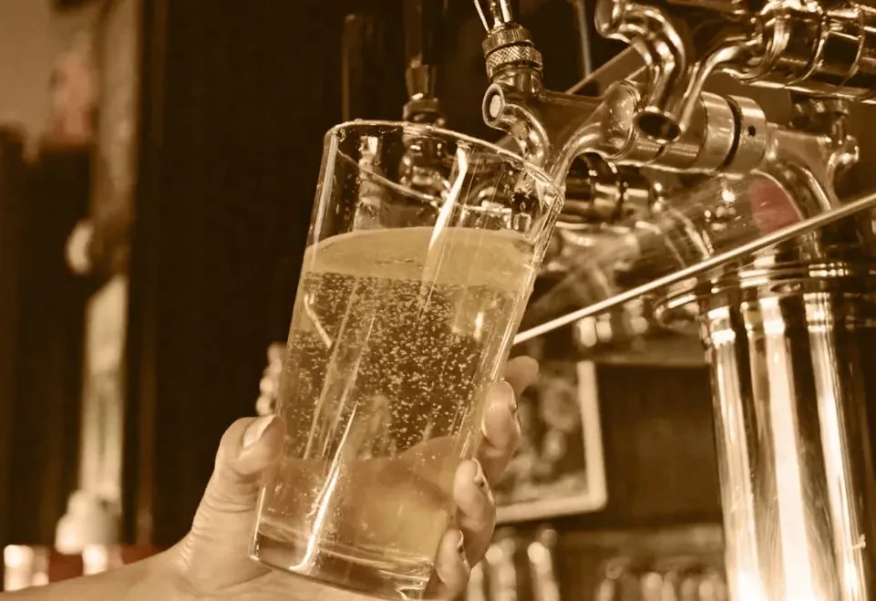 Sepia-toned hand filling a glass with effervescent drink from tap.