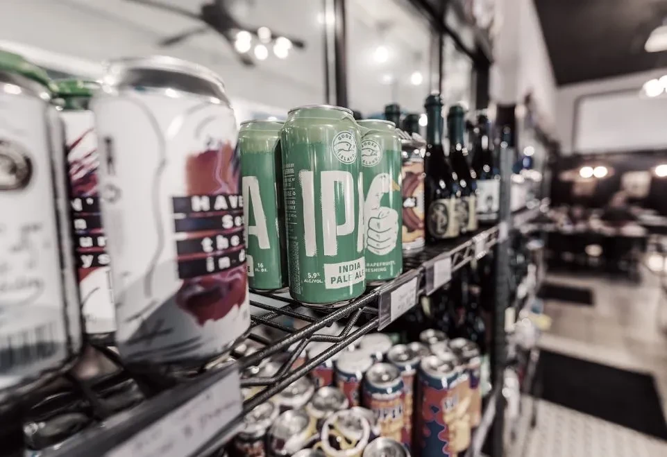 Retail shelf with Goose Island AIPA cans and assorted bottled drinks.