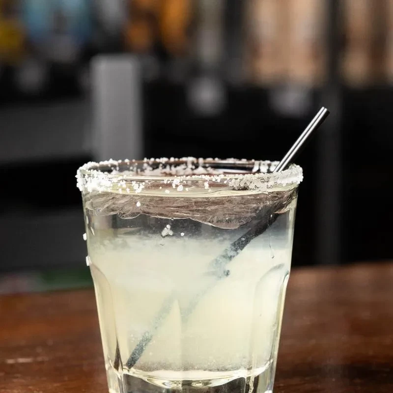 Salt-rimmed cocktail in a faceted glass with dark straw.