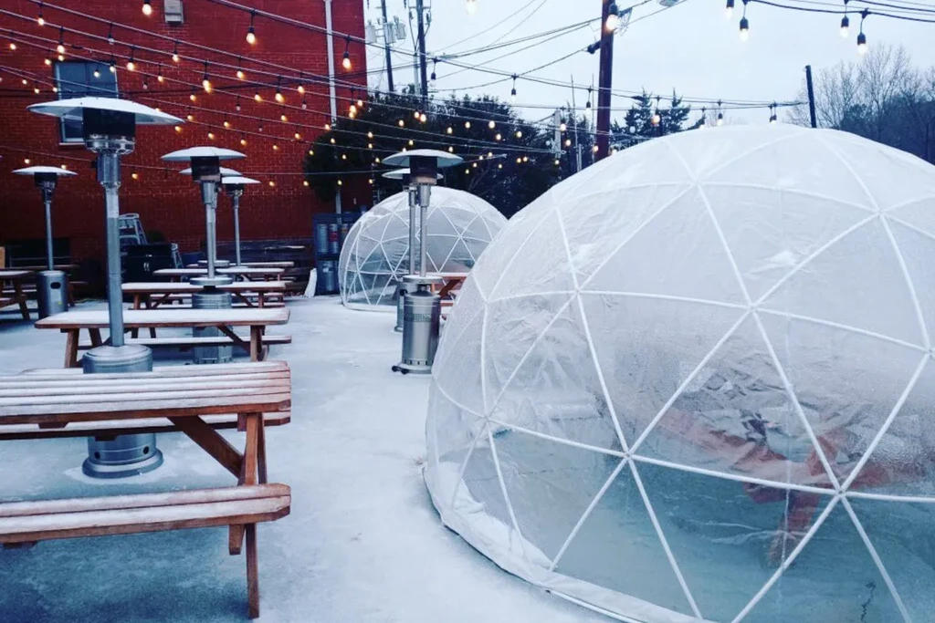 Outdoor winter dining with transparent igloo domes, snow, and patio heaters.