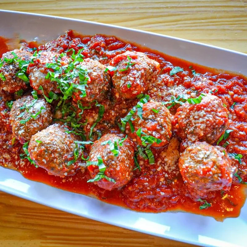 Browned meatballs in chunky red tomato sauce with cheese and fresh herbs.